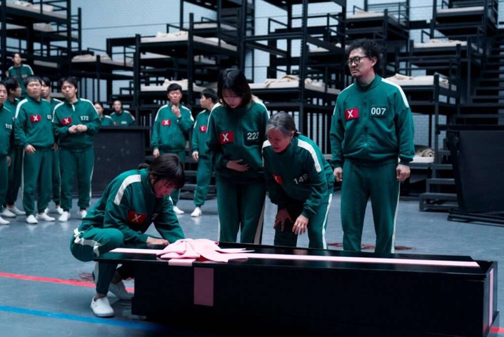  Several people in green uniforms stand near a large box, capturing a scene from Squid Game Season 3's dramatic tension.