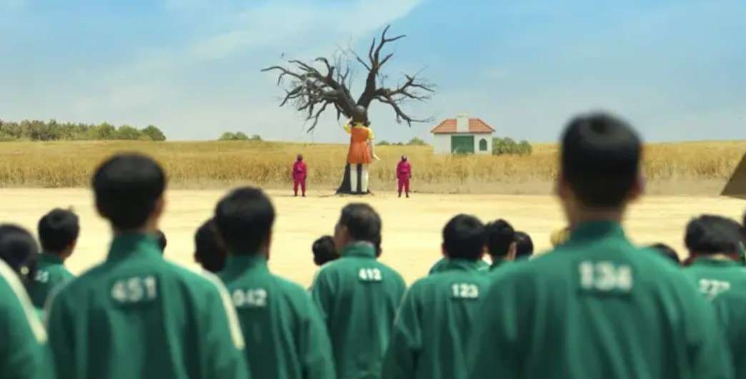 A group of individuals in green uniforms stands together in a field, referencing Squid Game Season 1's intense atmosphere.