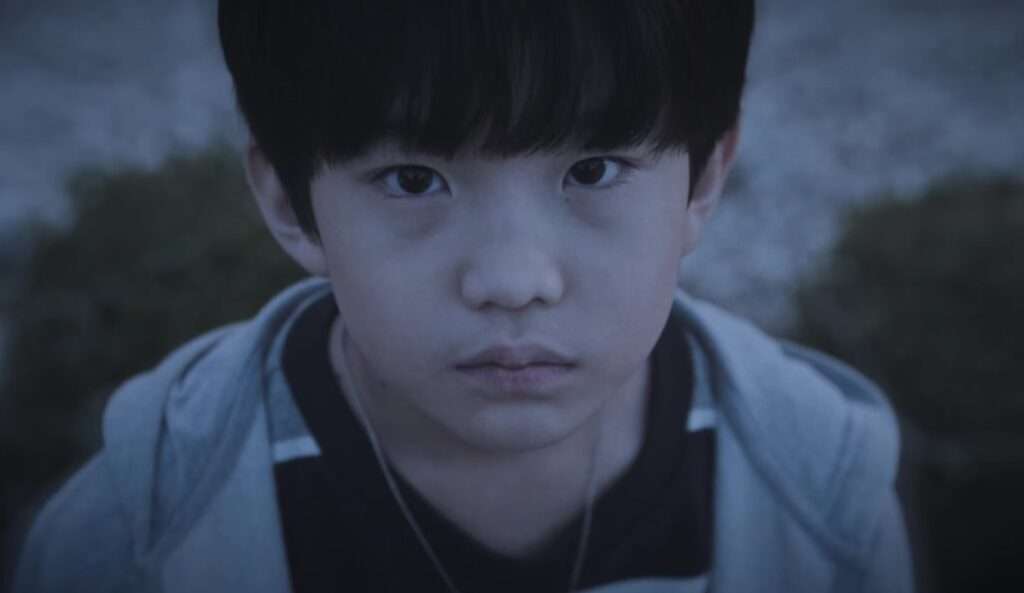 A young character from the Blind full review wearing a hoodie, gazing intently in a dimly lit outdoor setting, adding to the mysterious and suspenseful tone of the Korean drama.