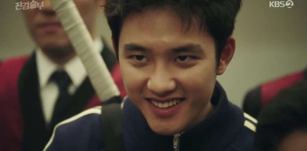 Close-up scene from Bad Prosecutor full review featuring Doh Kyung-soo as Jin Jung smiling confidently, with a baseball bat and other characters in the background, showcasing a key moment from the K-drama on KBS2.