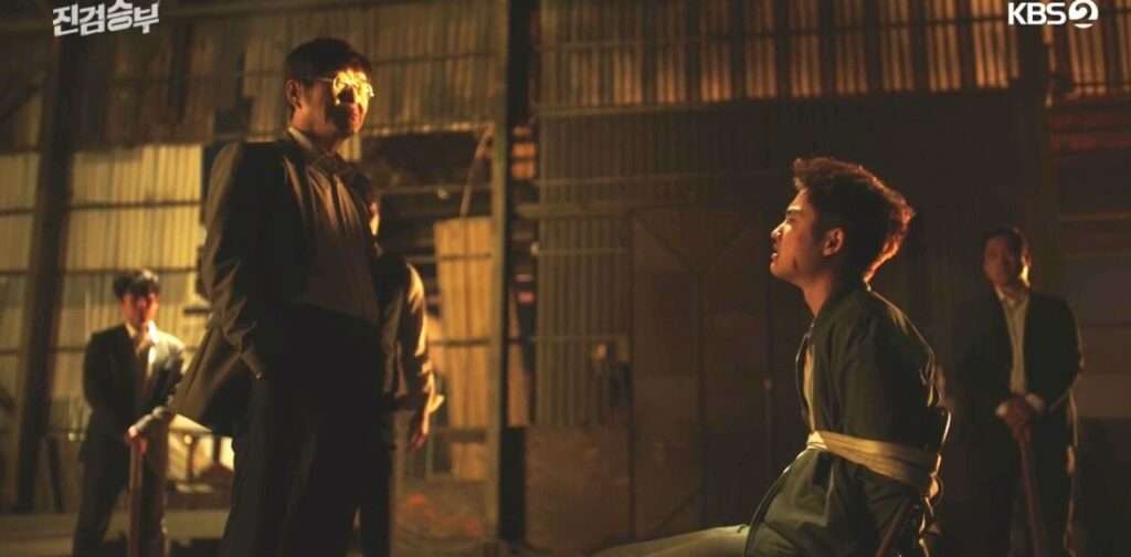  From "Bad Prosecutor," a man is seated on the ground, and another man stands beside him, creating a dramatic scene.