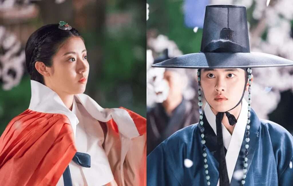 Dramatic scene from Korean drama 100 Days My Prince showing the female lead in a red and white hanbok and the Crown Prince in a blue hanbok with a traditional gat, under a backdrop of falling petals – 100 Days My Prince full review