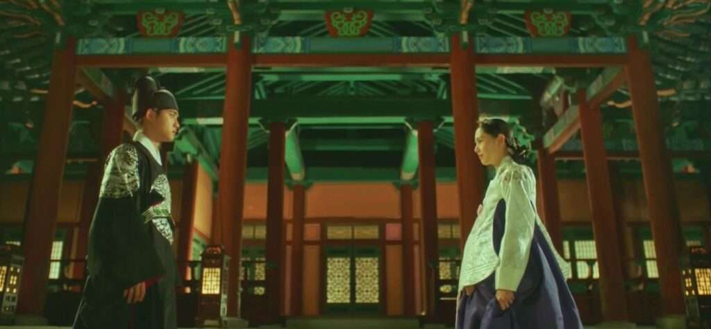Two people dressed in traditional clothing stand before a building, highlighting cultural significance and architectural style. 