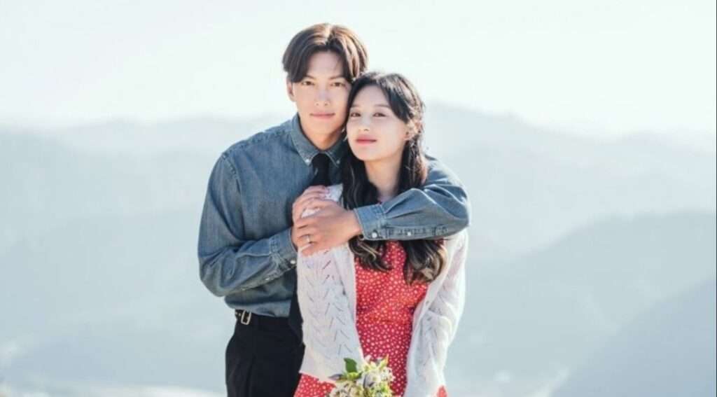 A romantic embrace between the leads of Love Struck in the City against a scenic mountain backdrop, holding flowers, showcasing the K-drama's tender moments