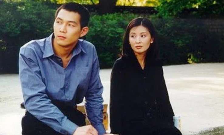 Lee Jung-jae and Lee Mi-sook sitting on a bench in an outdoor scene from 'An Affair', part of his Lee Jung-jae profile and biography.