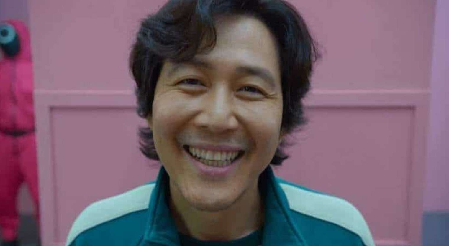 Lee Jung Jae smiles in front of a vibrant pink wall, showcasing a cheerful and inviting atmosphere.