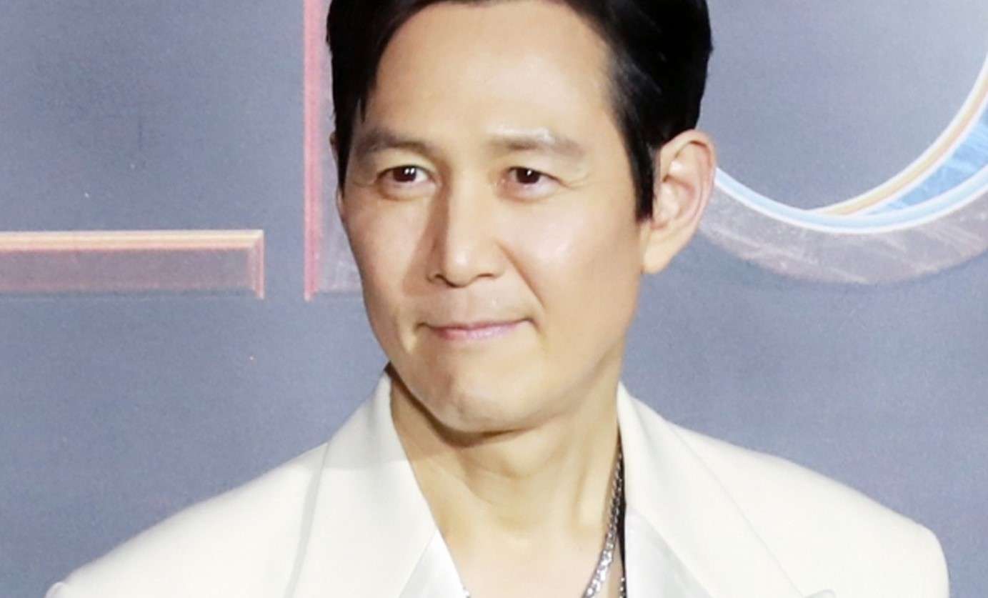 Lee Jung Jae stands confidently in a tailored white suit and shirt, embodying a chic and modern aesthetic.