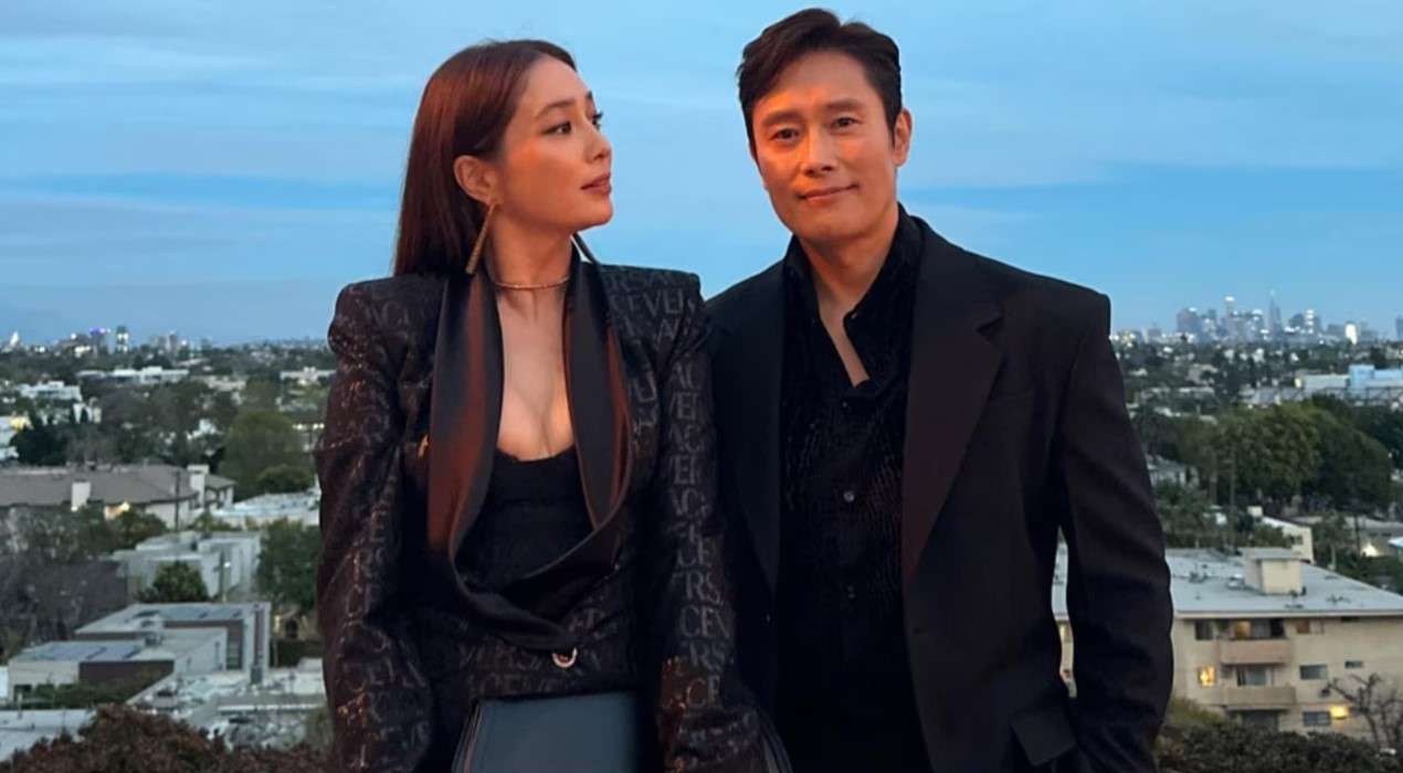 Lee Byung Hun and his wife on a rooftop, engaged in conversation about Lee Byung-hun's profile and biography. 
