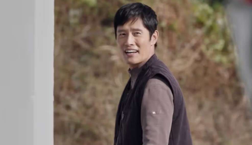 Lee Byung-hun, dressed in a vest, smiles while walking, showcasing his charismatic presence in Lee Byung Hun profile and biography. 