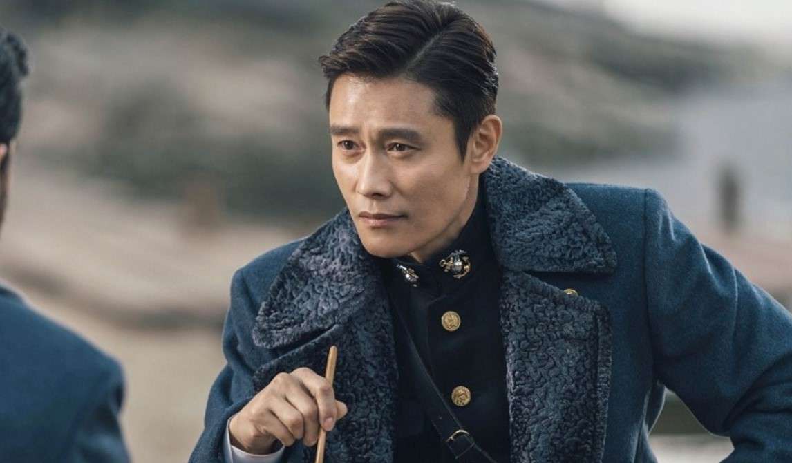Lee Byung-hun in a blue coat converses with another man, highlighting his engaging personality and presence.