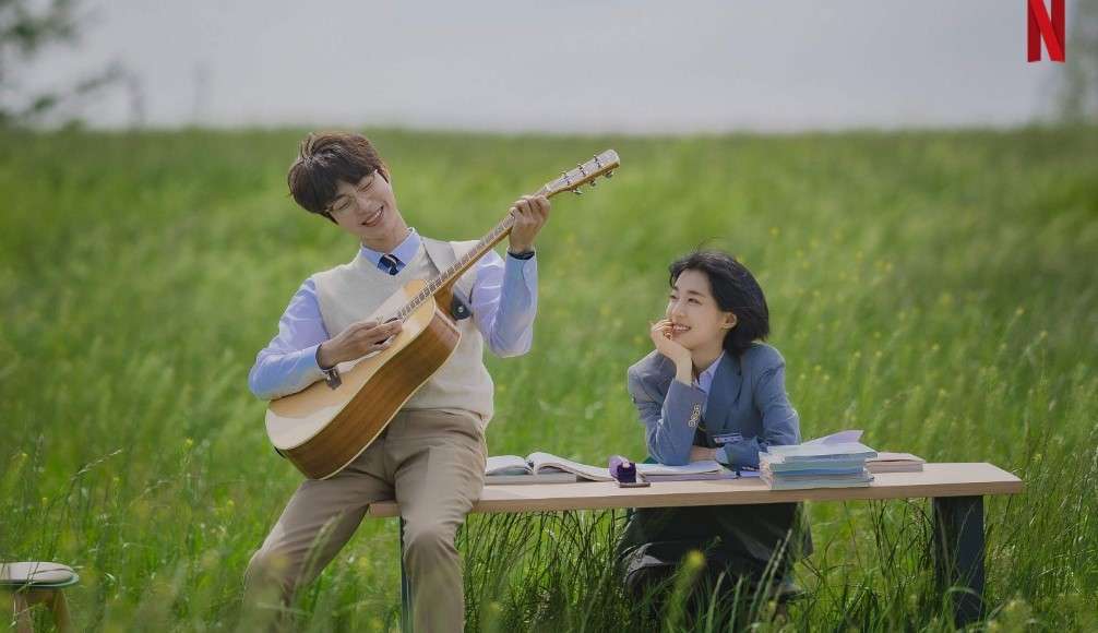 Two characters from "The Sound of Magic" in a serene field, one playing a guitar and the other reading, with books on a bench, Netflix logo visible.