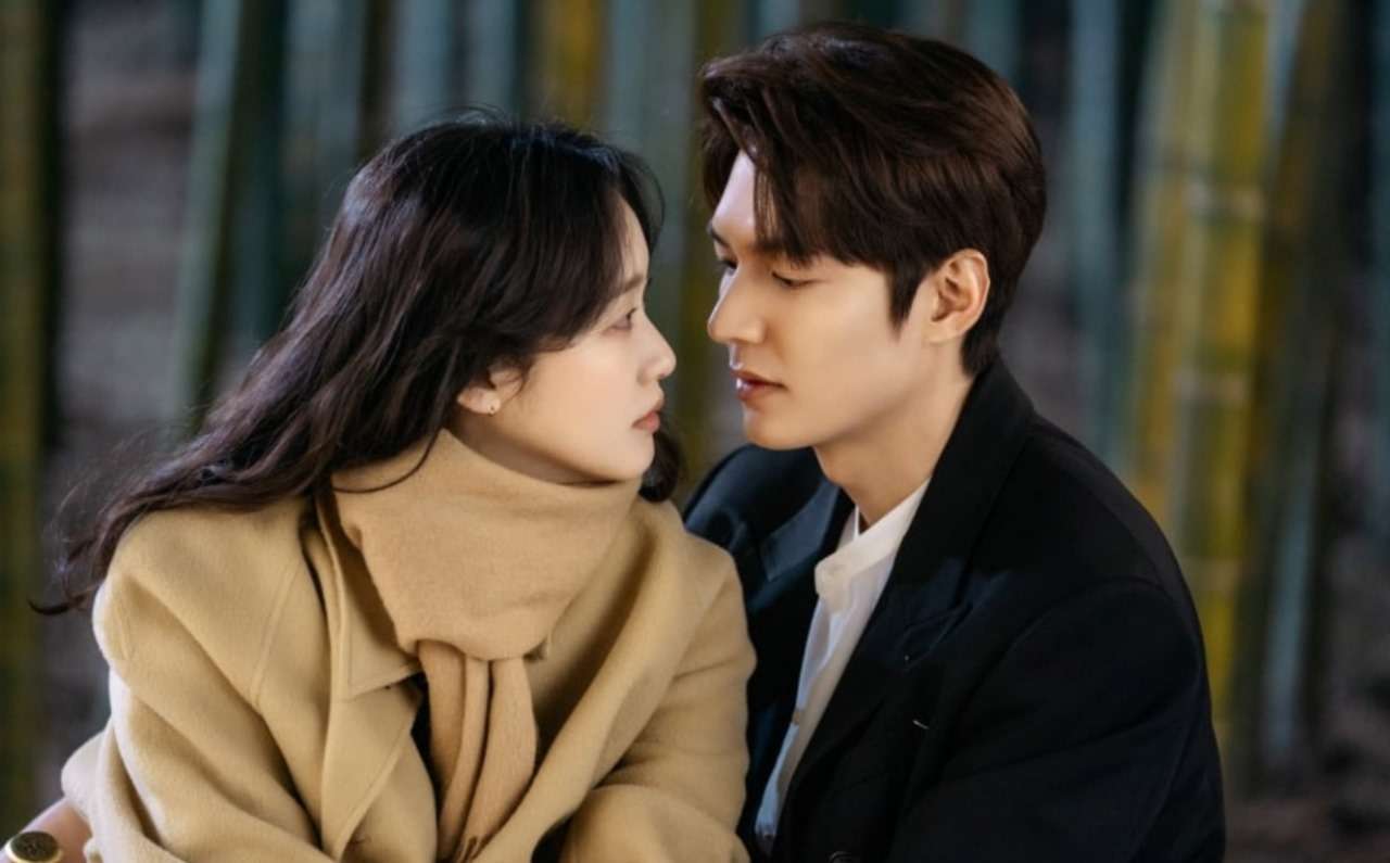 Romantic close-up of a couple in warm winter clothing, a woman in a beige coat and a man in a black suit, facing each other amidst a serene bamboo forest background.