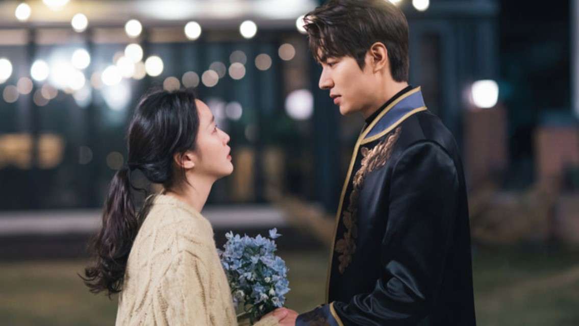 Romantic scene from "The King: Eternal Monarch" featuring a couple holding hands, one with a bouquet of blue flowers, set against a softly lit outdoor background.