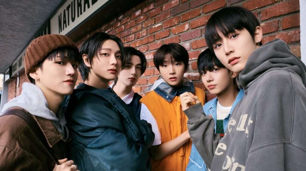 BOYNEXTDOOR K-pop group members Sungho, Riwoo, Jaehyun, Taesan, Leehan, and Woonhak posing stylishly against a brick wall with a 'NATURAL' sign, capturing the boy-next-door vibe of Hallyu fashion trends