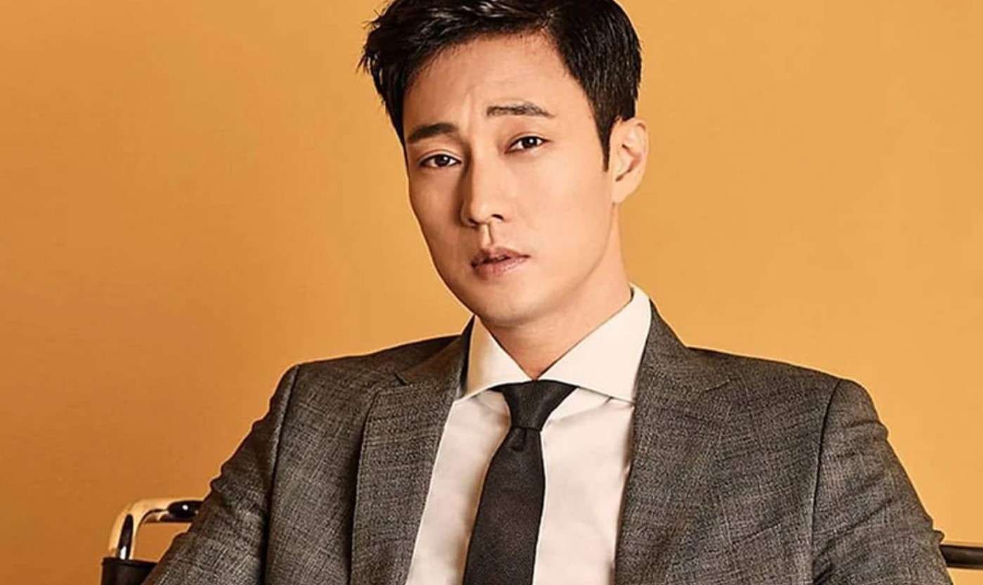 So Ji Sub in a stylish suit against an orange background, offering a glimpse into his professional persona for So Ji Sub profile and biography