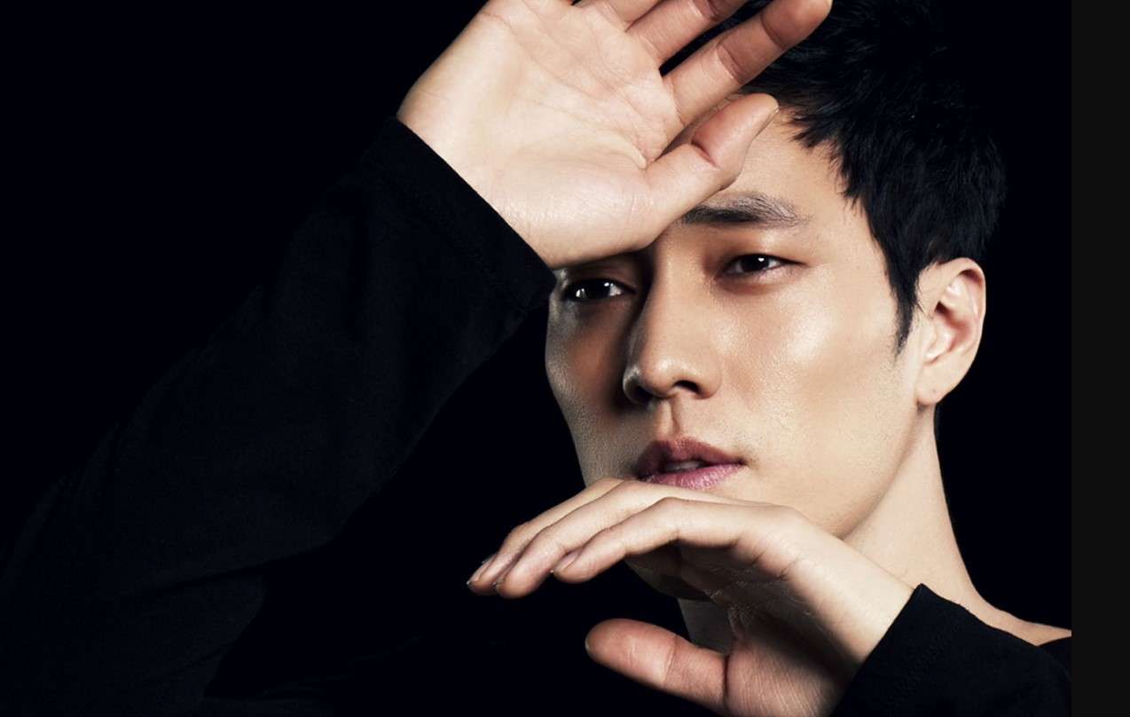 So Ji Sub in a dramatic close-up pose with hands framing his face against a black background, highlighting his intense expression and K-drama charisma