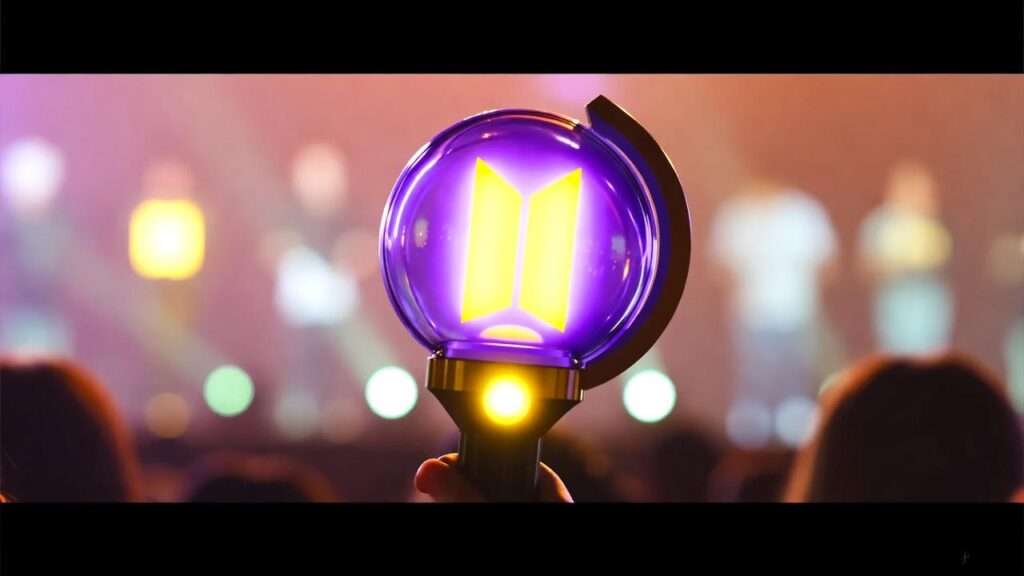 BTS Army Bomb light stick glowing at a vibrant K-Pop concert with a blurred crowd.