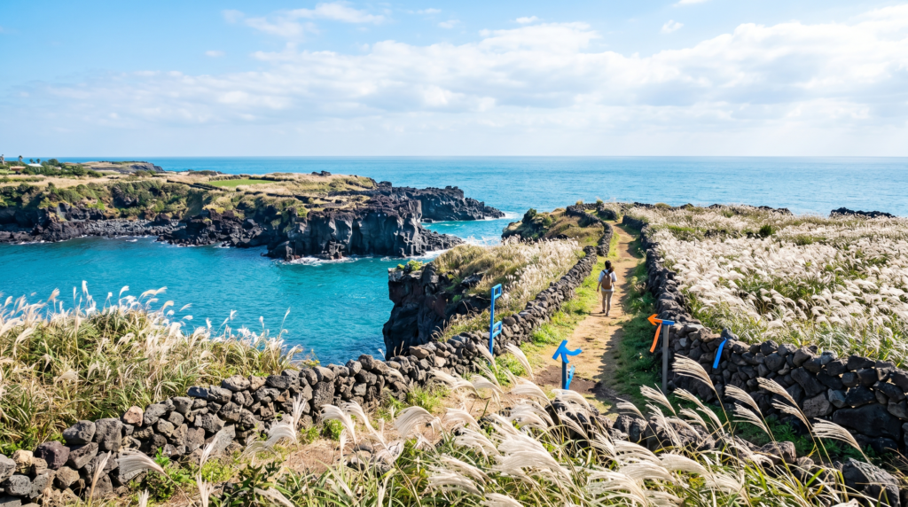 Solo hiker walking the Jeju Olle Trail along volcanic black lava cliffs above turquoise sea on Jeju Island South Korea